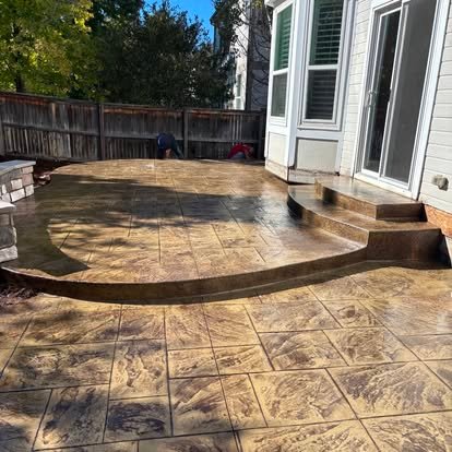 Curved stamped concrete patio with raised steps — large stone tile pattern viewed from behind home